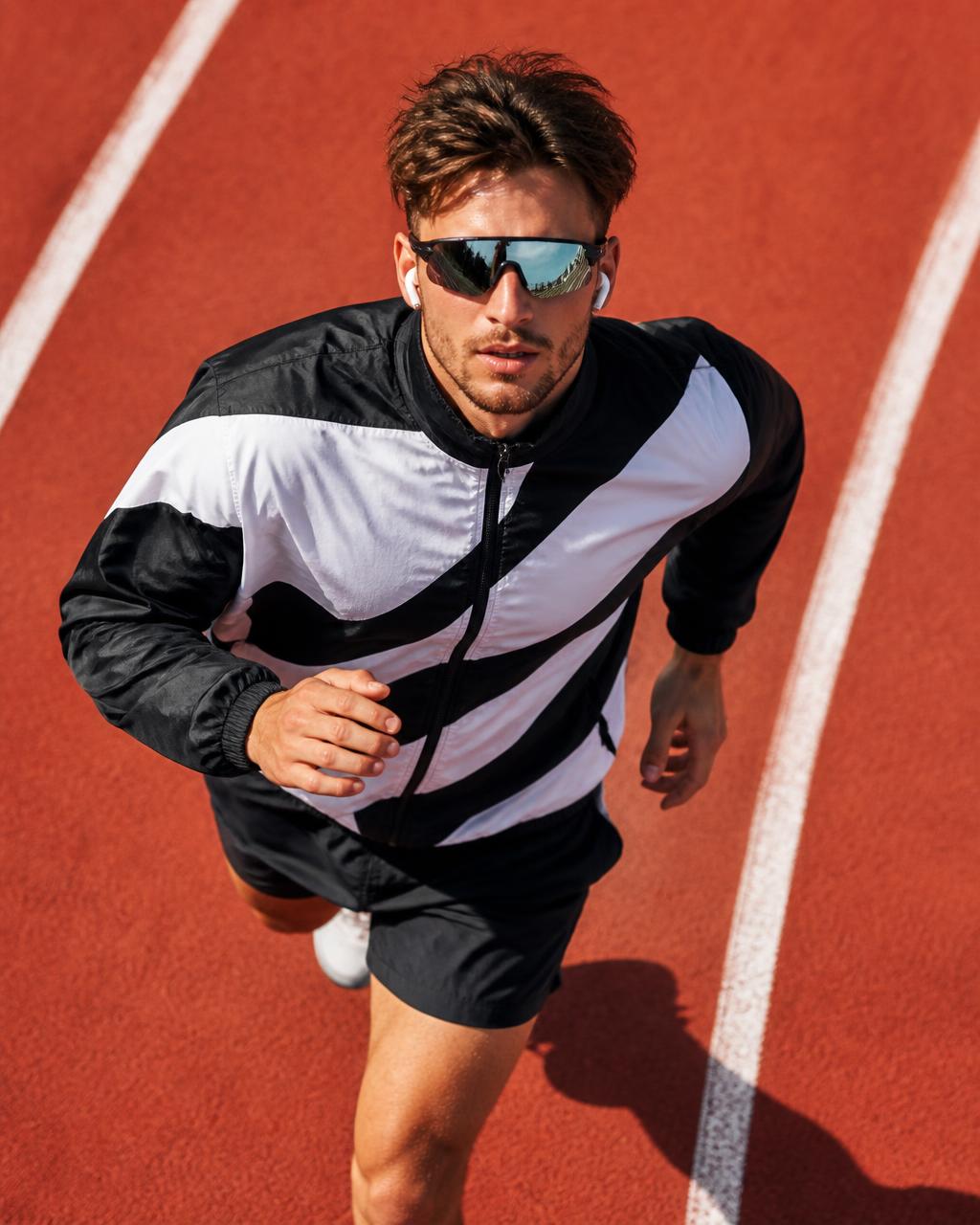 Runner in a black and white jacket crossing a terracotta track